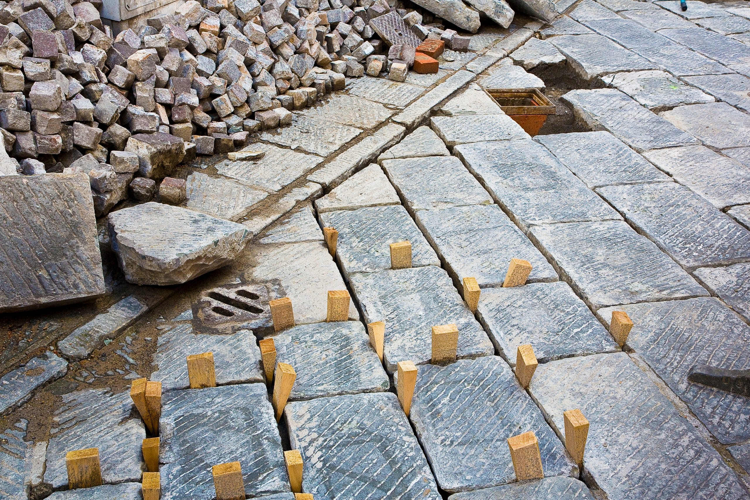 Stone pavement under repair with cobblestones stacked and wooden spacers in place.