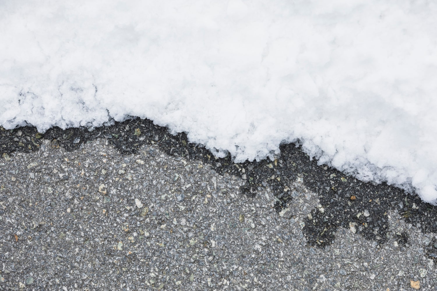 Snow partially covering a section of asphalt pavement, creating a clear line between ice and road.