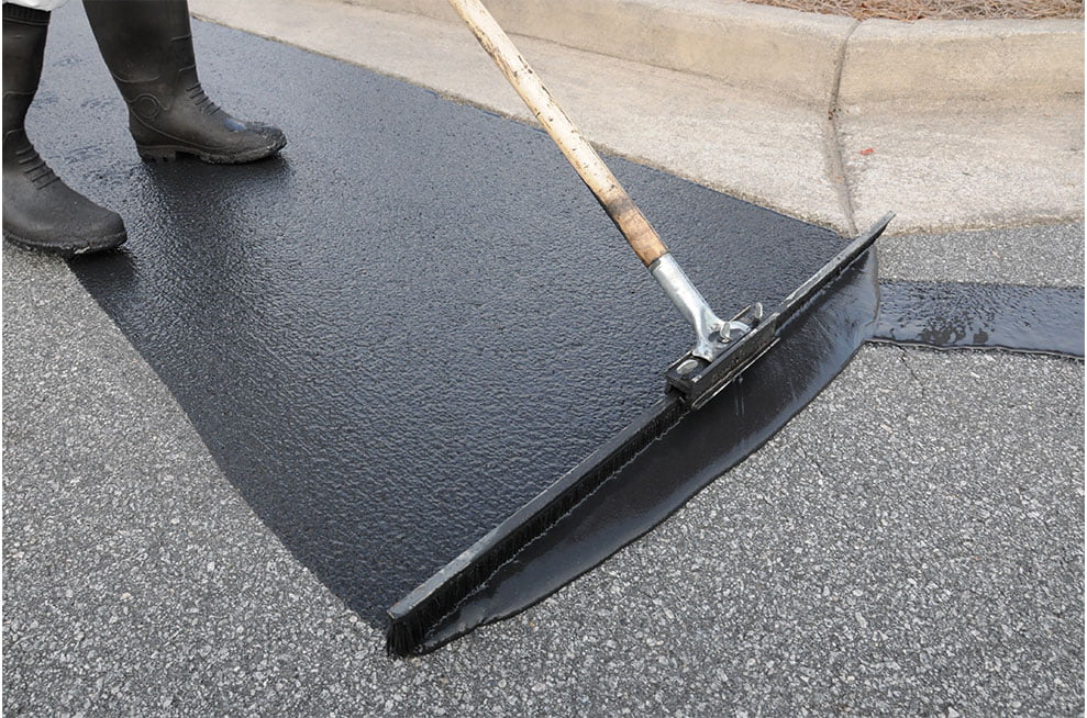 Person smoothing fresh black asphalt on a road with a large squeegee near a curb.