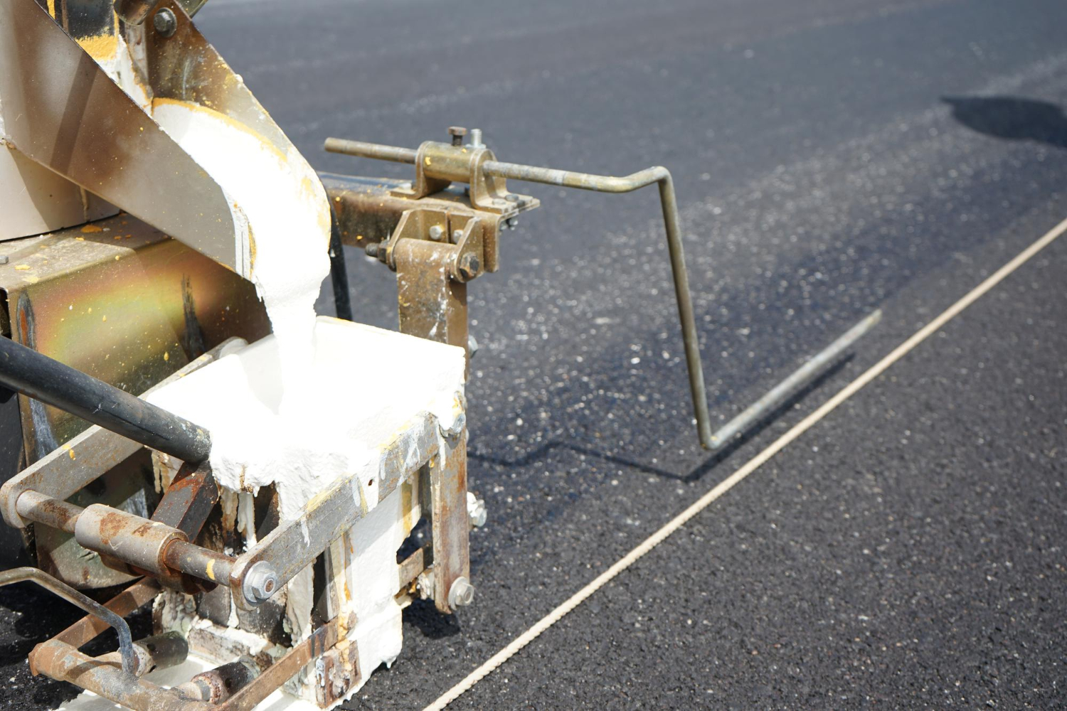 Machine applying white paint to create a straight road line on fresh asphalt pavement.
